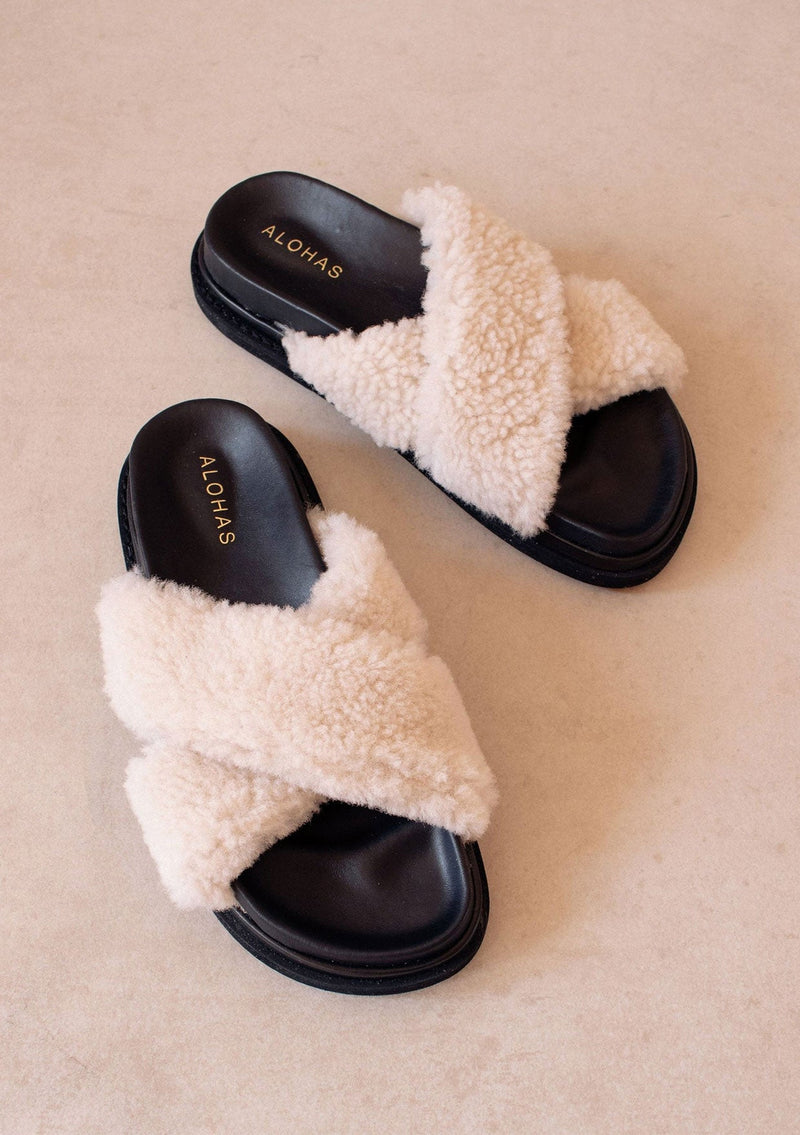 [Color: Black] Alohas cozy slipper cloud black sandals. Featuring a double layered chunky sole and white criss crossed straps made of fluffy natural shearling.