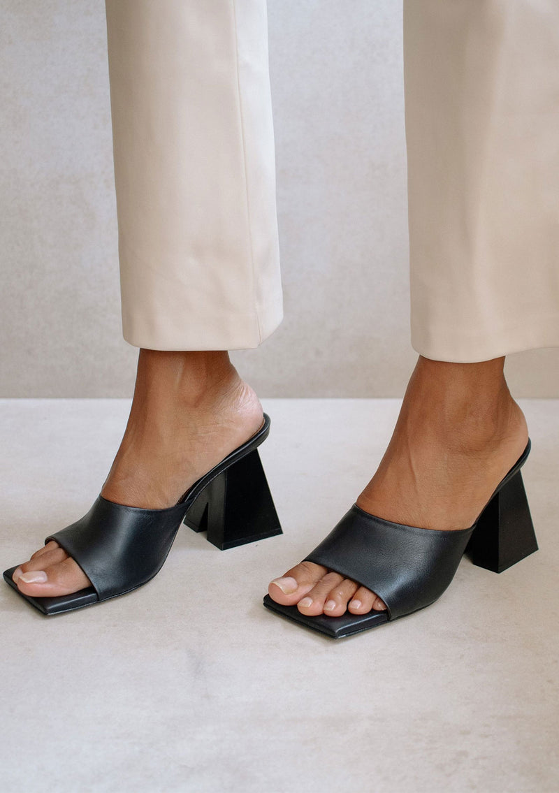 [Color: Black] Alohas classic black leather slip on mule dune sandal with a statement pyramid block heel. 