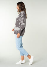 [Color: Charcoal/Silver] A side facing image of a brunette model wearing a bohemian cotton grey sweater with a silver floral motif. With long sleeves and a crew neckline.