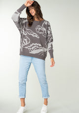 [Color: Charcoal/Silver] A front facing image of a brunette model wearing a bohemian cotton grey sweater with a silver floral motif. With long sleeves and a crew neckline.