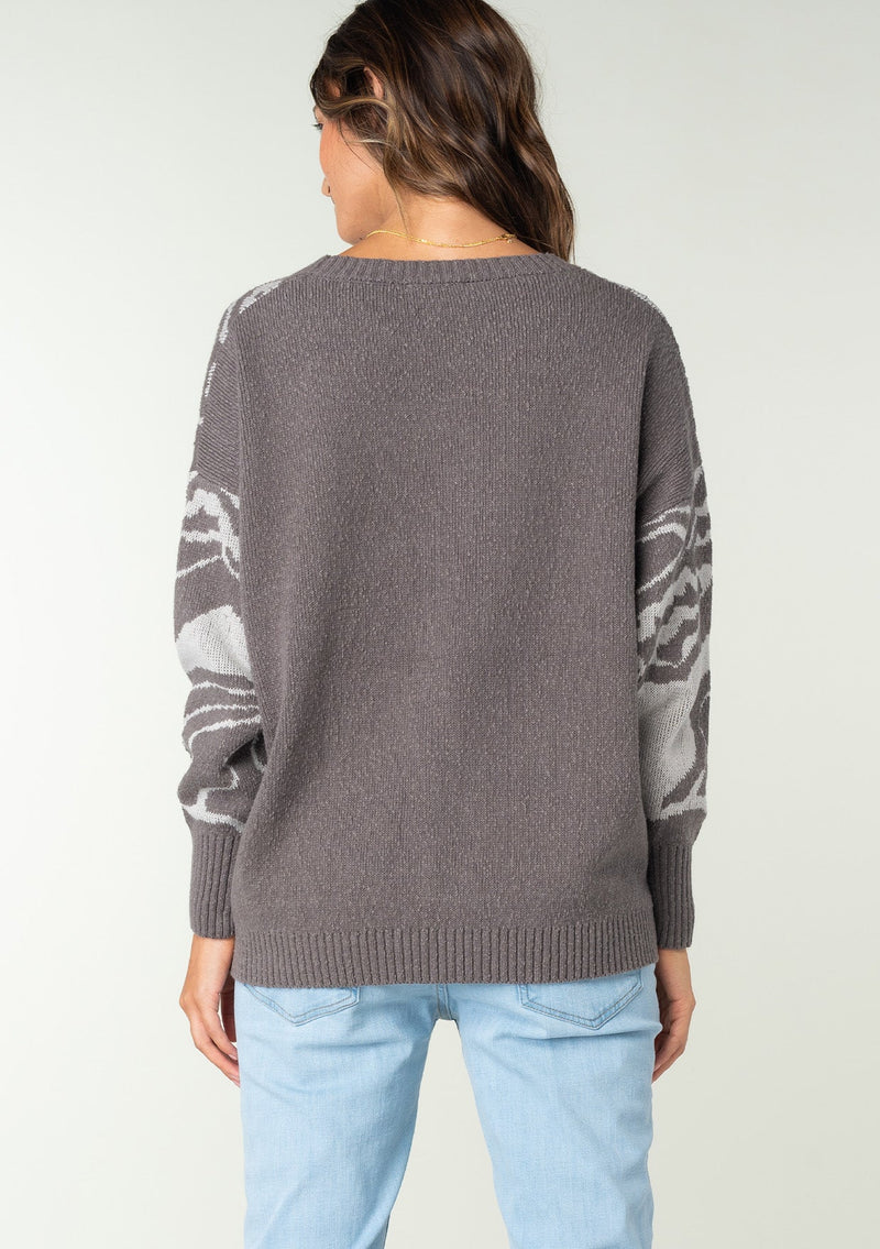 [Color: Charcoal/Silver] A back facing image of a brunette model wearing a bohemian cotton grey sweater with a silver floral motif. With long sleeves and a crew neckline.
