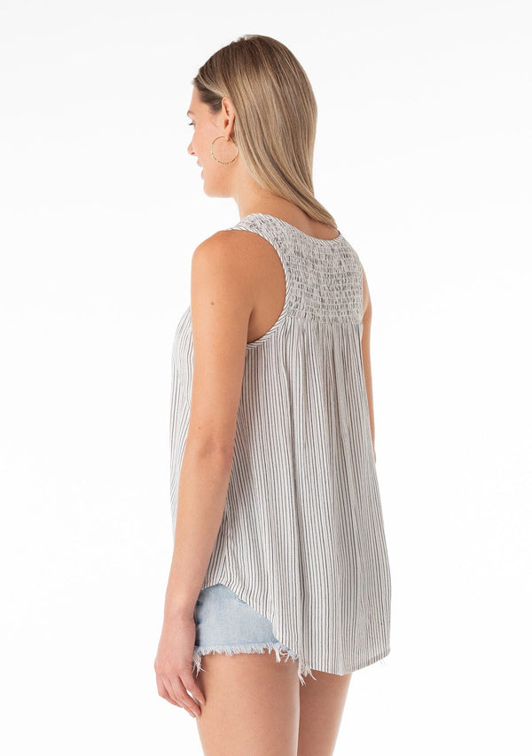 [Color: Off White/Black] An angled back facing image of a blonde model wearing a casual bohemian spring tank top in an off white and black stripe. With a v neckline, a smocked yoke detail, and a relaxed fit. 
