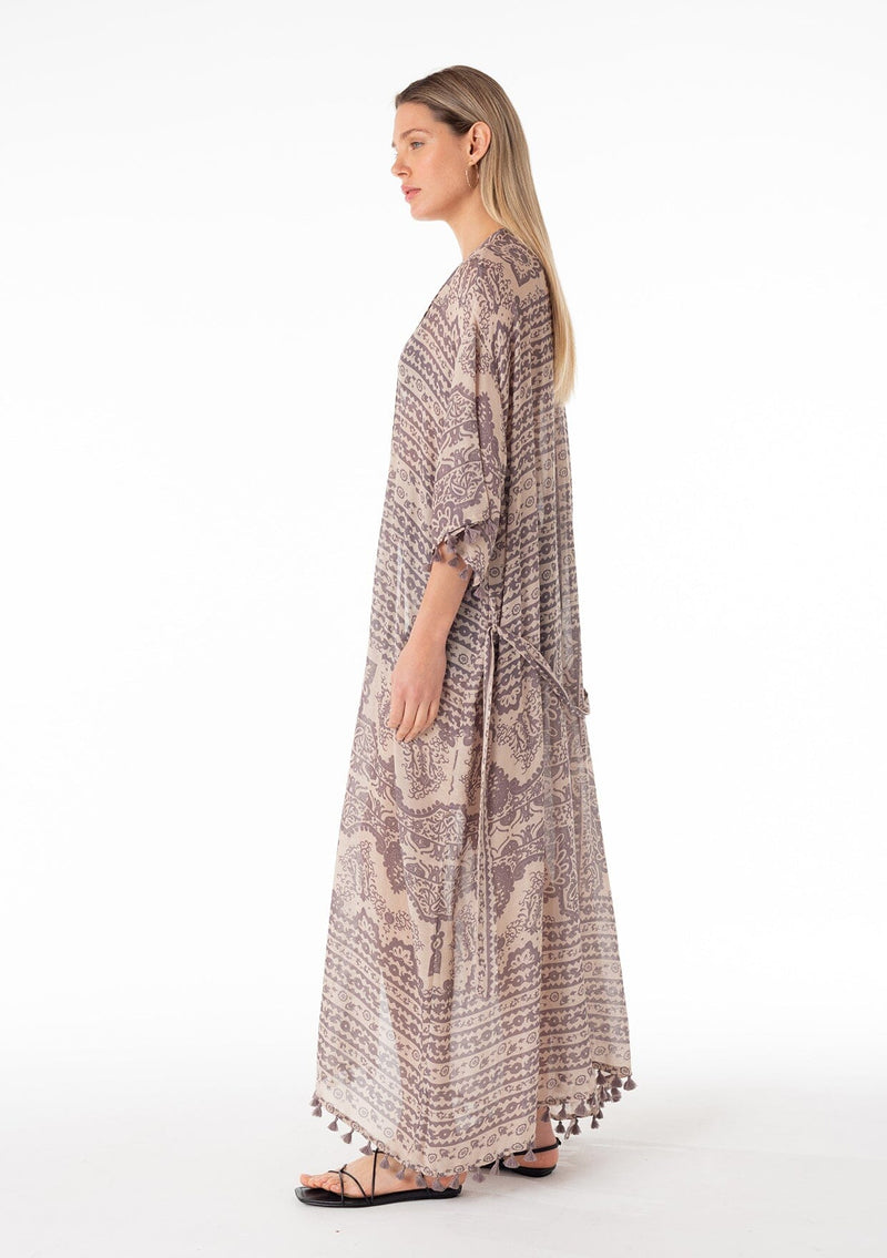 [Color: Natural/Grey] A side facing image of a blonde model wearing a bohemian lounge duster kimono robe in a grey mixed floral print. With short kimono sleeves, a tassel trimmed hemline, an open front, and a tie waist belt. 