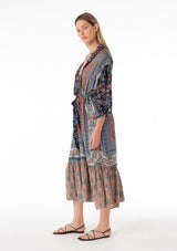 [Color: Teal/Navy] A side facing image of a blonde model wearing a bohemian mid length duster lounge robe in a mixed blue floral print. With half length long sleeves, a tiered ruffle trimmed hemline, an open front, and a tie waist belt. 
