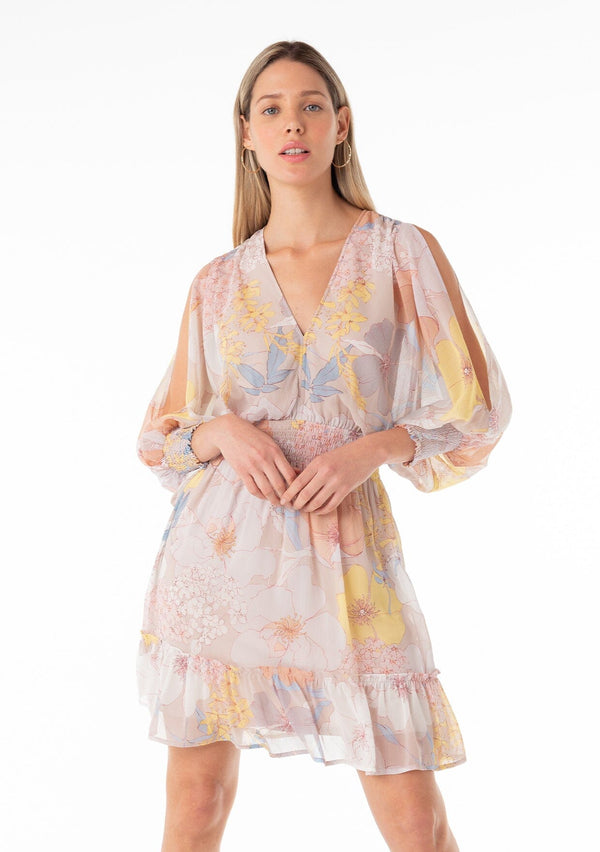 [Color: Natural/Blue] A front facing image of a blonde model wearing a best selling bohemian mini dress designed in a pink and blue floral print. With long split sleeves, a flowy tiered skirt, a smocked elastic waist, a v neckline, and an open back with tassel tie closure. 