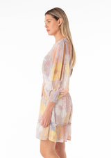 [Color: Natural/Blue] A side facing image of a blonde model wearing a best selling bohemian mini dress designed in a pink and blue floral print. With long split sleeves, a flowy tiered skirt, a smocked elastic waist, a v neckline, and an open back with tassel tie closure. 