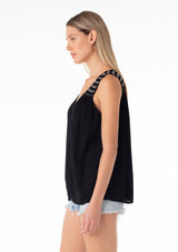[Color: Black/Ivory] A side facing image of a blonde model wearing a bohemian black tank top. With a v neckline in the front and back, a tassel tie closure at the back, a smocked yoke detail, and contrast embroidered stitch detail. 