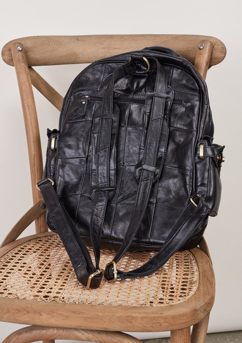 [Color: Black] Patchwork leather backpack with top handle and multiple outer pockets.