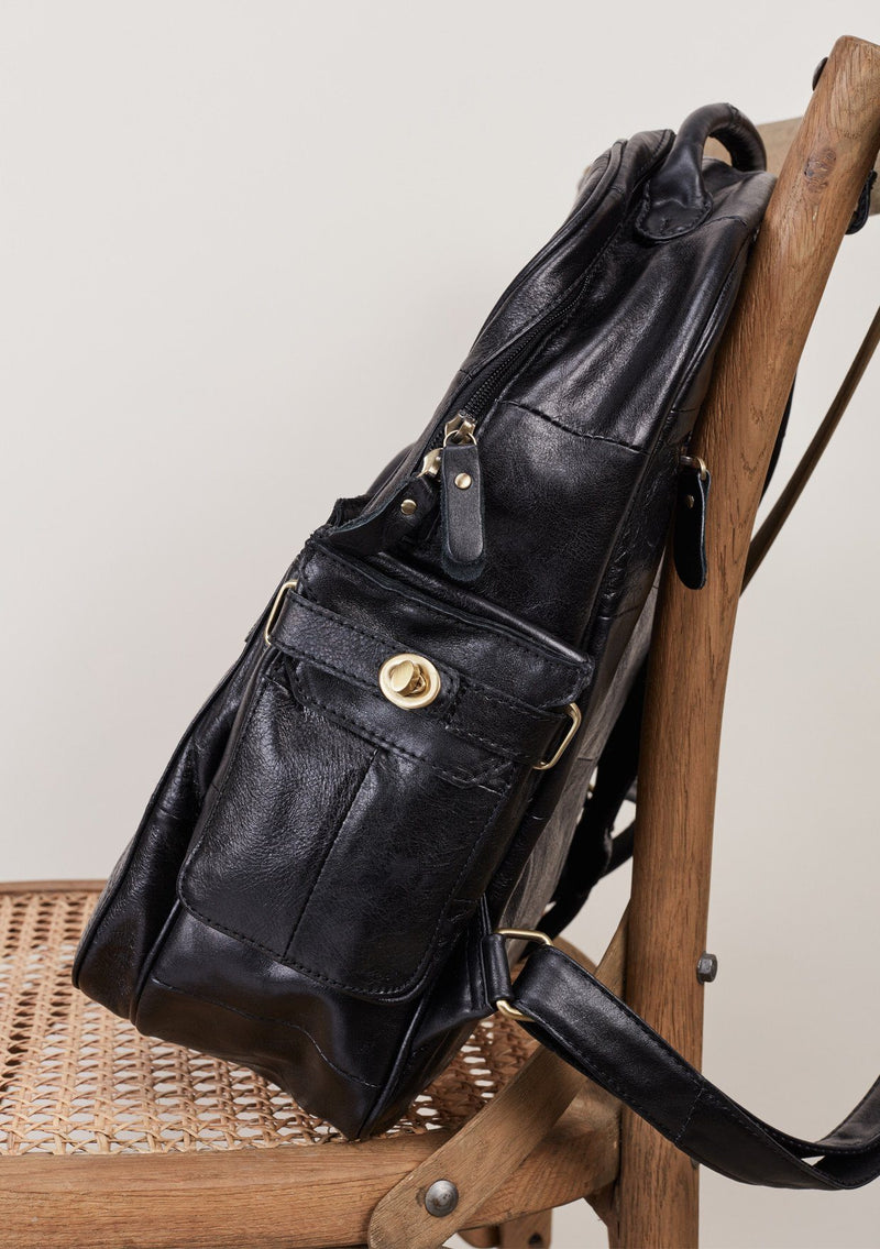 [Color: Black] Patchwork leather backpack with top handle and multiple outer pockets.