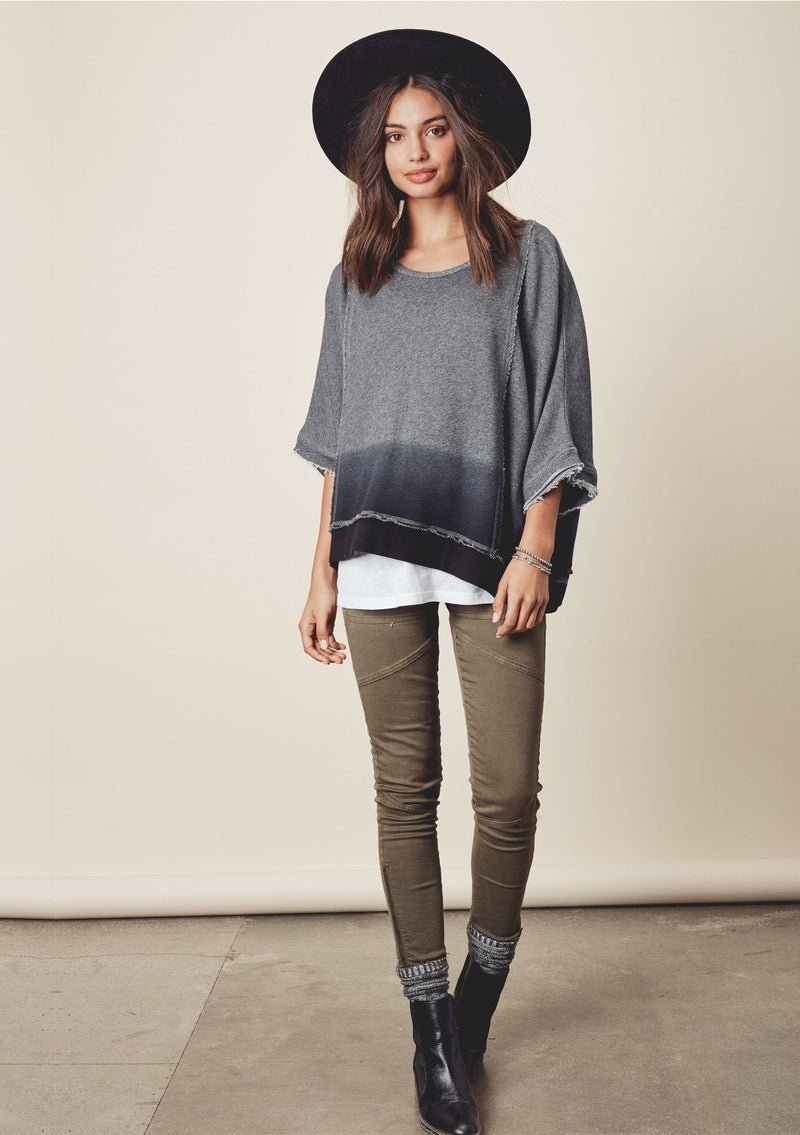 [Color: Charcoal/Midnight] A model wearing a relaxed grey dyed sweatshirt with a scoop neckline, long batwing sleeves, and raw edge finish details. 