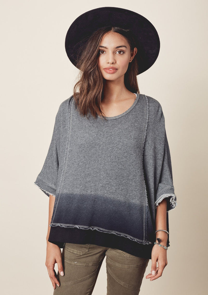 [Color: Charcoal/Midnight] A model wearing a relaxed grey dyed sweatshirt with a scoop neckline, long batwing sleeves, and raw edge finish details. 
