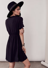 [Color: Black/Multi] A brunette model wearing a bohemian black dress with multicolored stripes and a tassel trim detail. Complete with a deep v-neckline, an elastic waist, and short sleeves. 