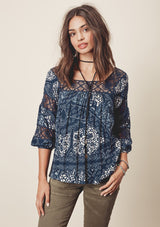 [Color: Teal/Vanilla] A front facing image of a brunette model wearing a teal  bohemian blouse with crochet lace trims. 