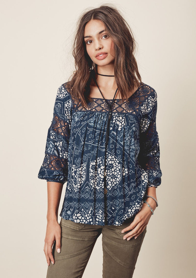 [Color: Teal/Vanilla] A front facing image of a brunette model wearing a teal  bohemian blouse with crochet lace trims. 