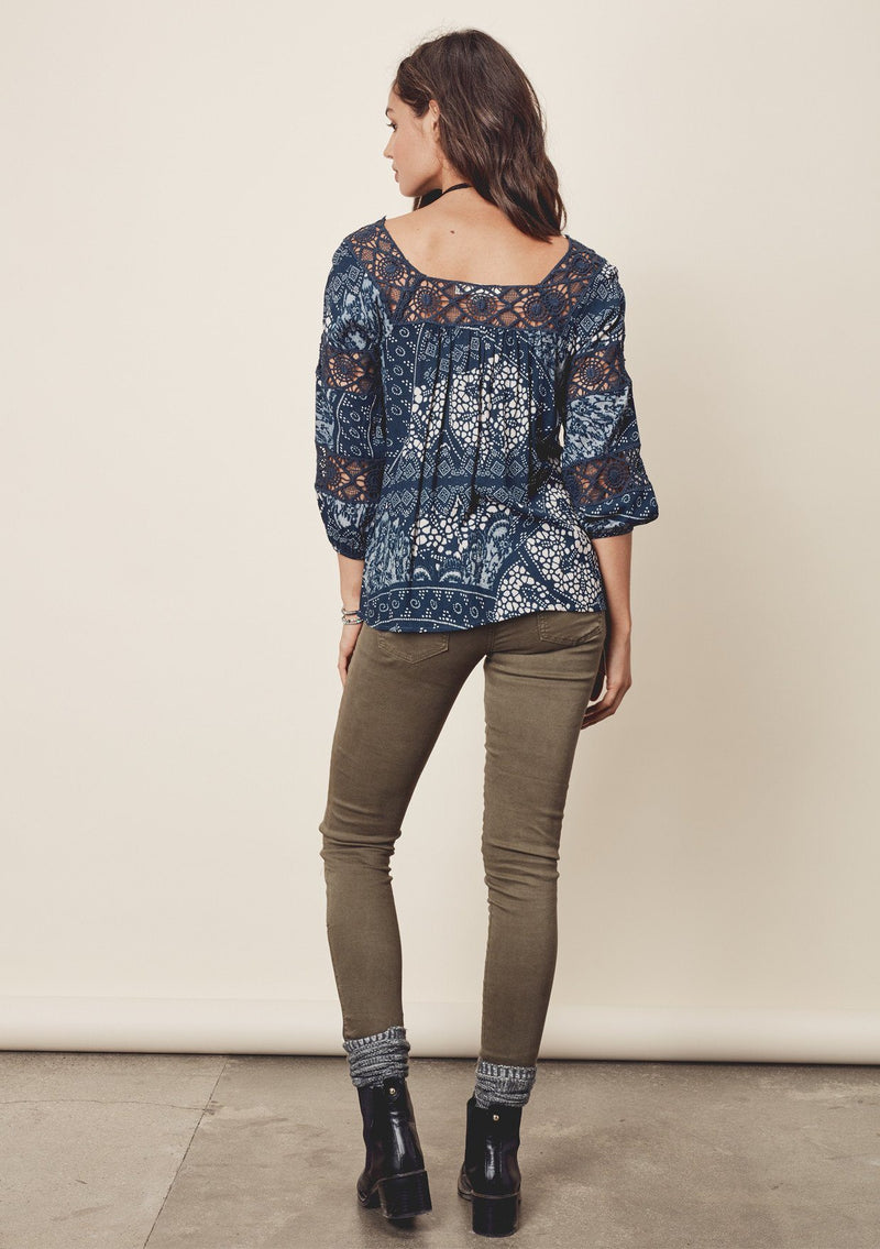 [Color: Teal/Vanilla] A back facing image of a brunette model wearing a teal  bohemian blouse with crochet lace trims. 