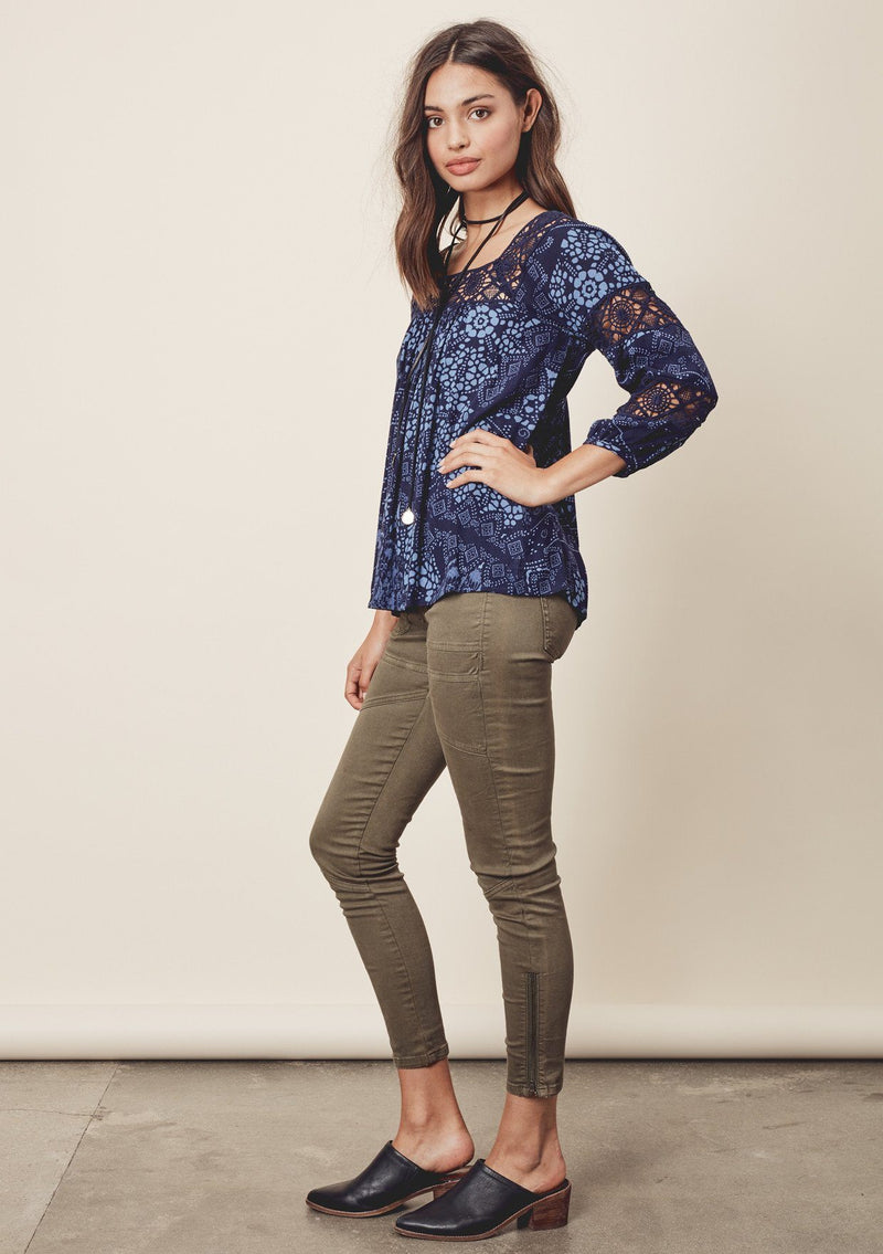 [Color: Midnight/Blue] A side facing image o a brunette model wearing a blue bohemian blouse with crochet lace trims. 