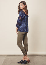 [Color: Midnight/Blue] A side facing image o a brunette model wearing a blue bohemian blouse with crochet lace trims. 