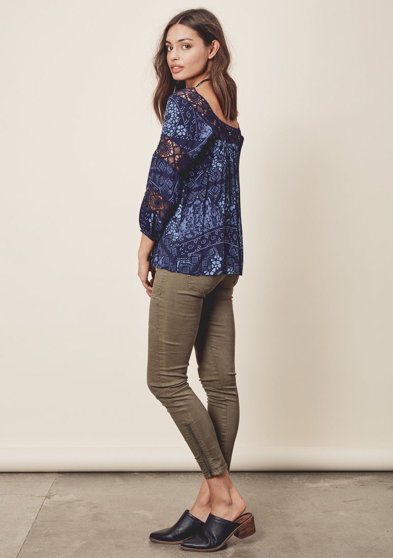 [Color: Midnight/Blue] A side facing image o a brunette model wearing a blue bohemian blouse with crochet lace trims. 