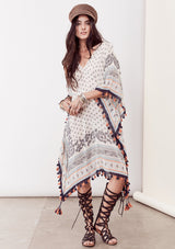 [Color: Ivory/Blue/Orange] A brunette model wearing a bohemian border print  caftan with tassel trim and a class v-neckline. A beach cover up or festival layer
