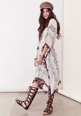 [Color: Ivory/Blue/Orange] A brunette model wearing a bohemian border print  caftan with tassel trim and a class v-neckline. A beach cover up or festival layer