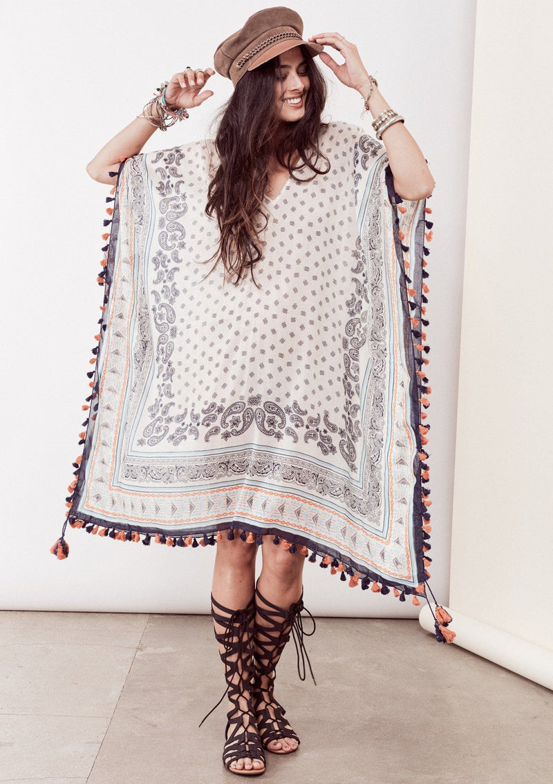 [Color: Ivory/Blue/Orange] A brunette model wearing a bohemian border print  caftan with tassel trim and a class v-neckline. A beach cover up or festival layer
