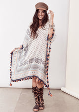 [Color: Ivory/Blue/Orange] A brunette model wearing a bohemian border print  caftan with tassel trim and a class v-neckline. A beach cover up or festival layer