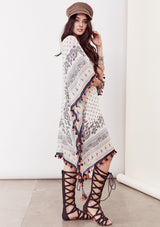 [Color: Ivory/Blue/Orange] A brunette model wearing a bohemian border print  caftan with tassel trim and a class v-neckline. A beach cover up or festival layer