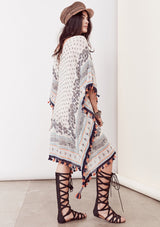 [Color: Ivory/Blue/Orange] A brunette model wearing a bohemian border print  caftan with tassel trim and a class v-neckline. A beach cover up or festival layer