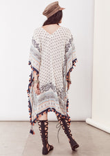 [Color: Ivory/Blue/Orange] A brunette model wearing a bohemian border print  caftan with tassel trim and a class v-neckline. A beach cover up or festival layer