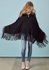 [Color: Black] A front facing image of a blonde model wearing a black suede fringed poncho. 