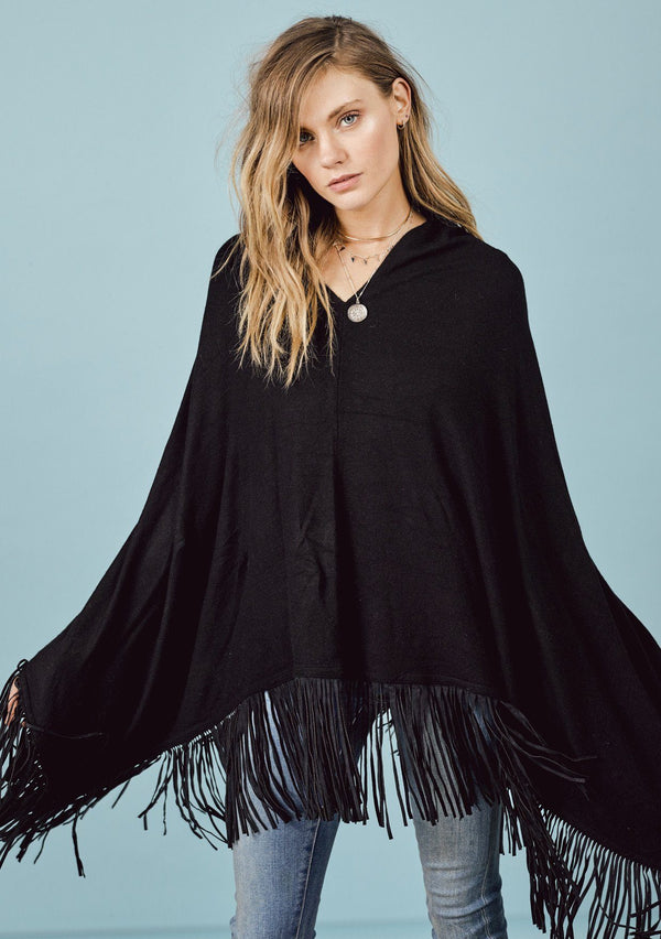 [Color: Black] A front facing image of a blonde model wearing a black suede fringed poncho.  