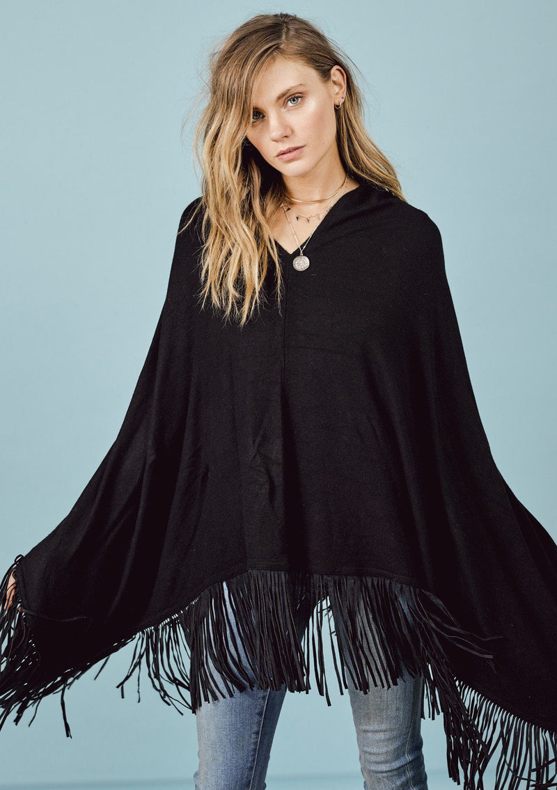 [Color: Black] A front facing image of a blonde model wearing a black suede fringed poncho.  
