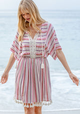 [Color: Natural/Pink] A model wearing a pink yarn dye stripe resort mini dress with tassel trim and crochet detail.