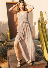 [Color: Red/Black] A woman outside wearing a striped sleeveless maxi dress with adjustable spaghetti straps with an o ring detail, an empire waist, and a v neckline. 