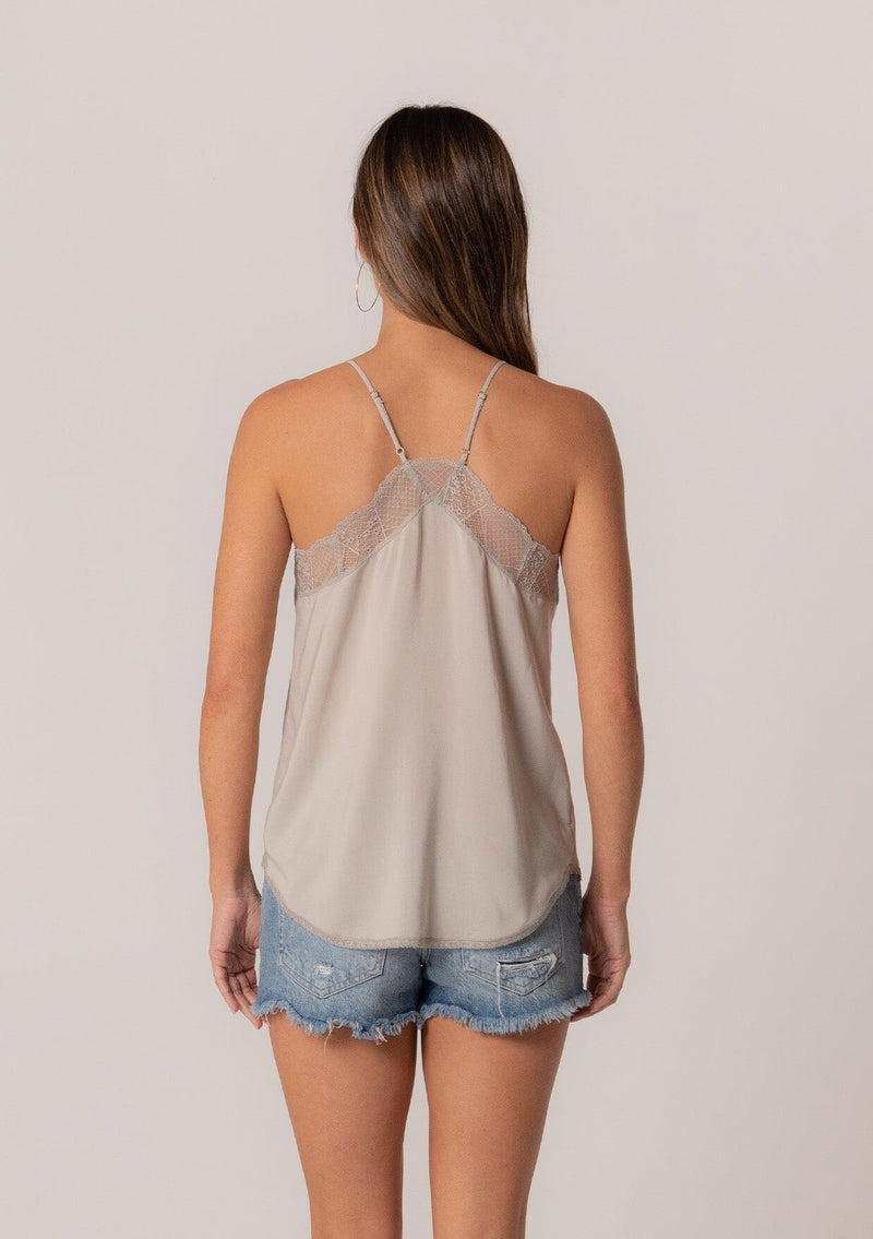 [Color: Mink] A back facing image of a brunette model wearing a light brown camisole tank top. With spaghetti straps, a v neckline, lace trim, a racerback, and a relaxed fit. 
