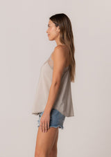 [Color: Mink] A side facing image of a brunette model wearing a light brown camisole tank top. With spaghetti straps, a v neckline, lace trim, a racerback, and a relaxed fit. 