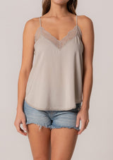 [Color: Mink] A close up front facing image of a brunette model wearing a light brown camisole tank top. With spaghetti straps, a v neckline, lace trim, a racerback, and a relaxed fit. 