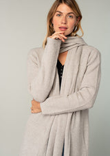 [Color: Mushroom] A model wearing a cozy taupe long shawl cardigan. With long sleeves, side pockets, an open front, and attached scarf detail.